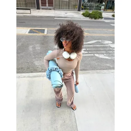 A Bala image ad: a creator on a pavement carrying a yoga mat, wearing the brand weights over a beige outfit