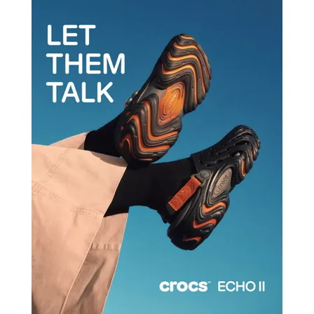 A Crocs ad creative: two legs kicked up against a blue sky wearing black Echo II clogs with orange swirled soles, under the line LET THEM TALK