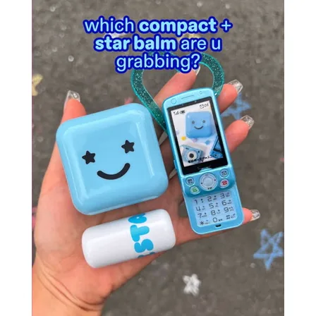 A Starface ad creative: a hand holding a blue smiley compact, a star balm and a blue flip phone over chalked pavement