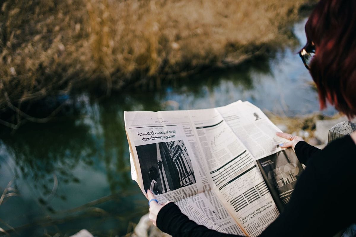 A person sits by the water and reads a folded newspaper: an advertorial competes for the same slow reading time, so it has to earn it
