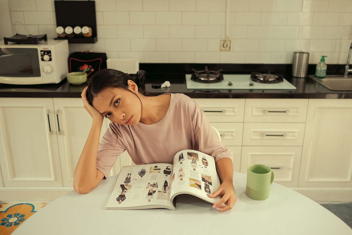 A woman at a kitchen table reads a magazine with her head on her hand: the reader trusts the page because it looks like reporting, which is why the label matters