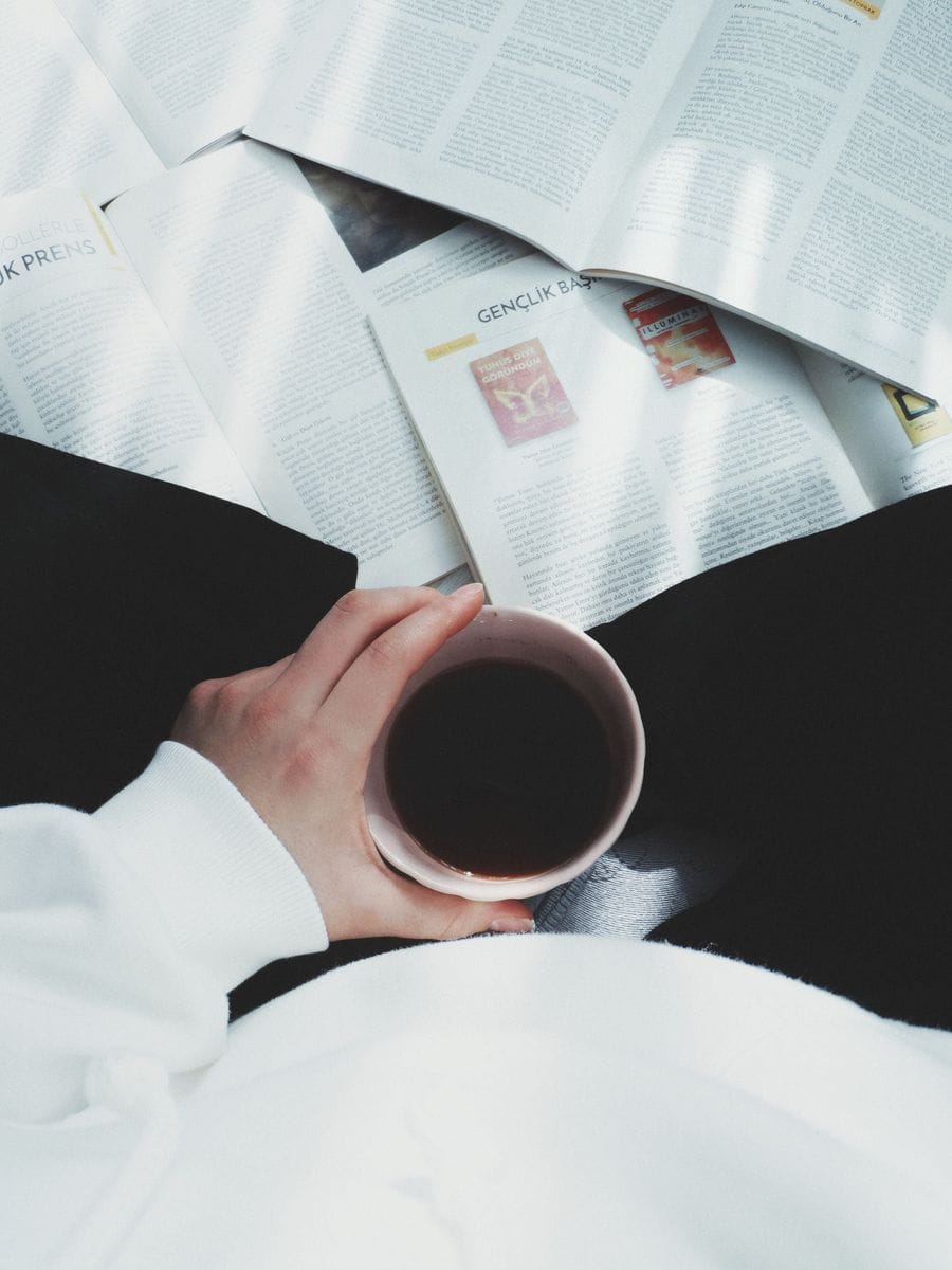 A hand holds a coffee cup among open magazines: the slow reading time an advertorial depends on, earned by the ad before it