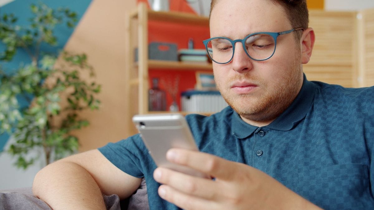 A man with glasses reads on his smartphone at home: the phone is where the advertorial is judged, so check the page there first