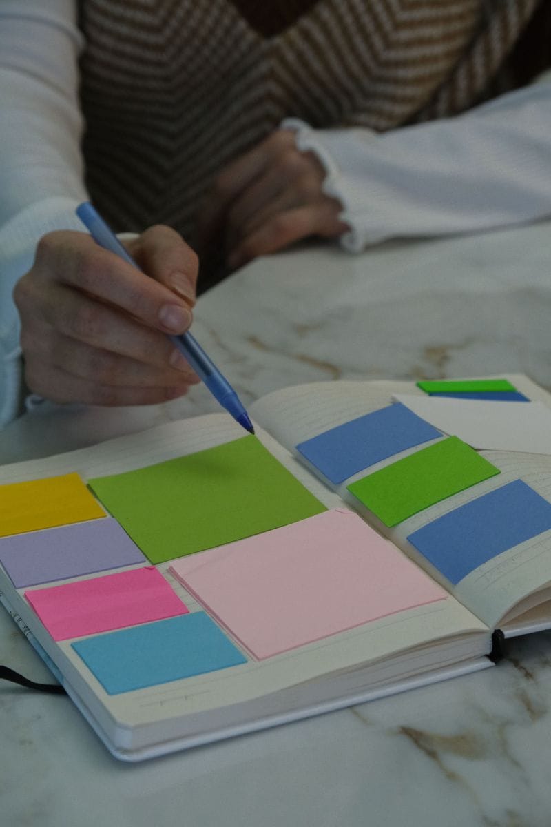 A pen points at colored sticky notes in an open notebook: plan the nine blocks on paper before anyone writes a sentence