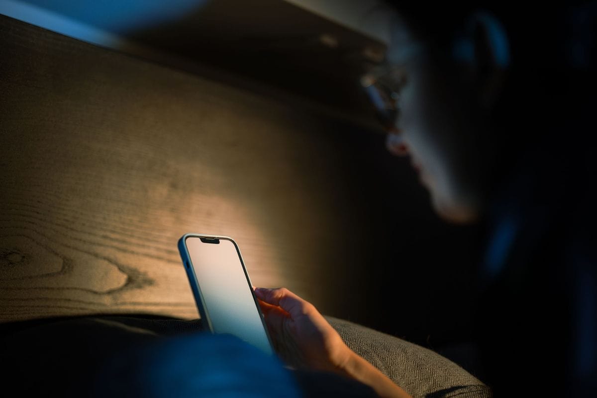 A phone screen lights up a dark room while someone reads in bed: late-night readers are the ones a good advertorial holds to the end