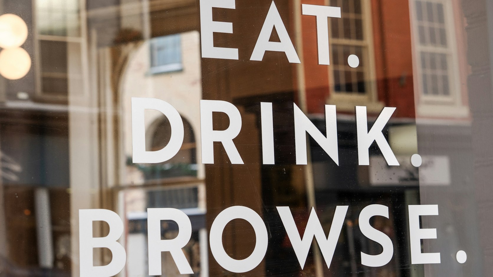 EAT. DRINK. BROWSE. painted in bold capitals on a shop window, three words and three full stops carrying a whole brand voice