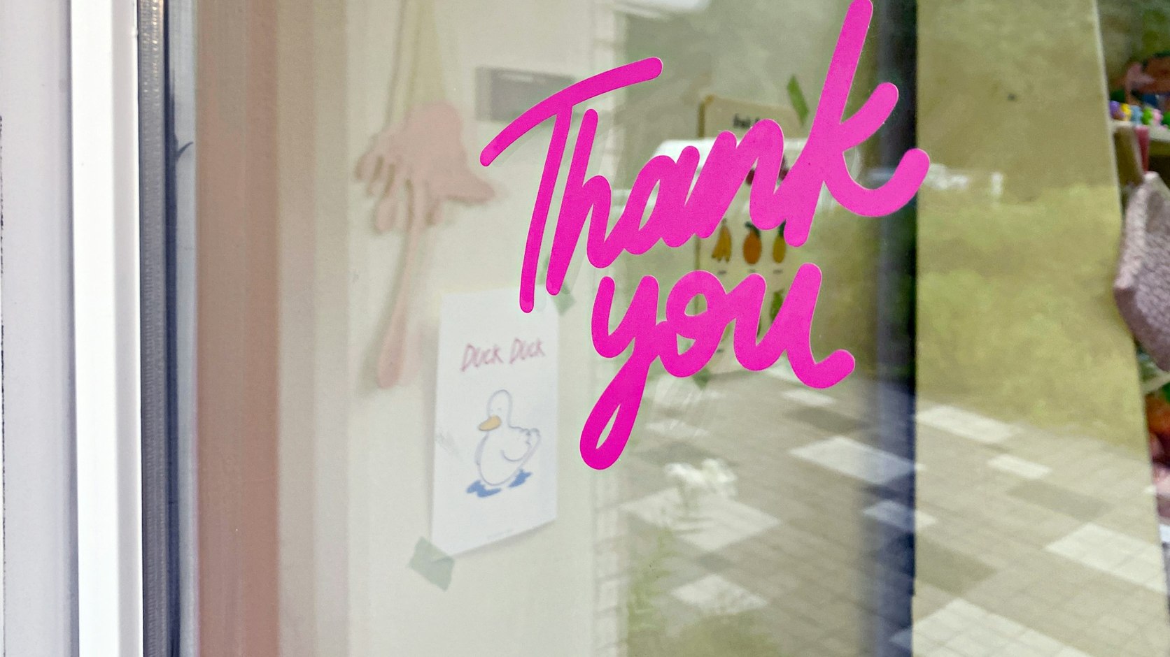 Thank you hand-painted in pink brush script across a shop window: the warm register out in the world, not in a brand deck