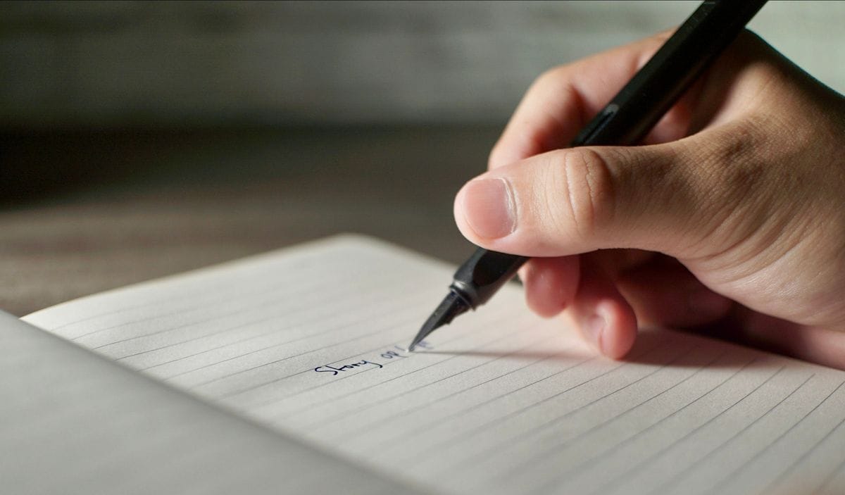 A hand writes a first draft with a black pen on lined paper: every example below started as a draft someone was willing to test