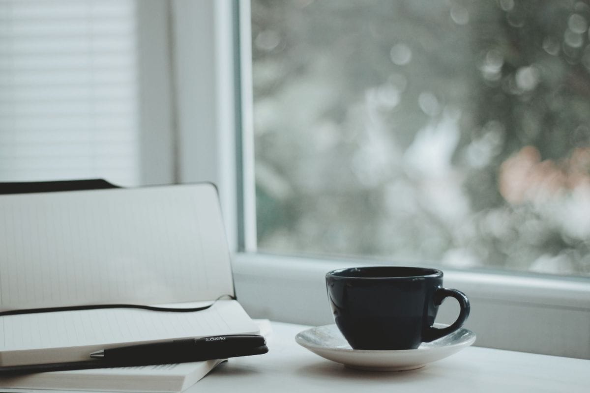 A closed notebook and a cup of coffee by a bright window: a voice guide short enough to remember before the writing session starts