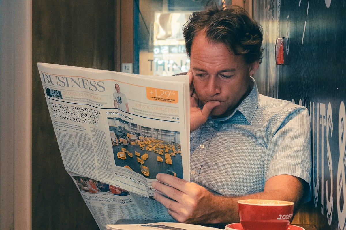 A man reading a printed newspaper at a cafe table with a coffee: the full-page print ad is where Patagonia told readers not to buy
