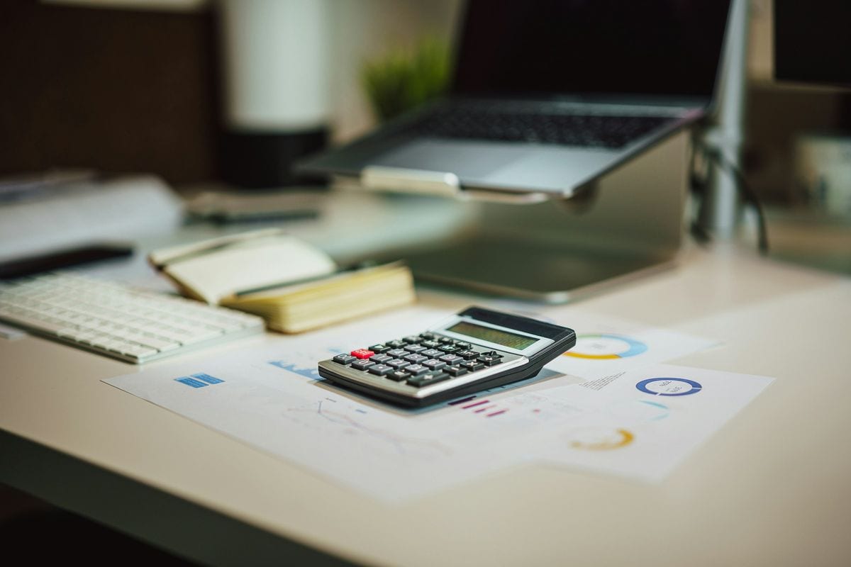 A calculator on a desk next to printed charts and a laptop: break-even ROAS starts with the cost lines of one order