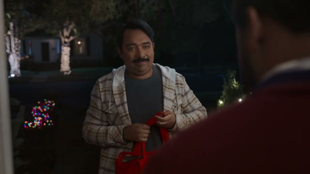 A frame from DoorDash's 2024 No One Has to Know holiday ad: a Dasher holds a red DoorDash bag at a front door at night, with Christmas lights in the yard behind him