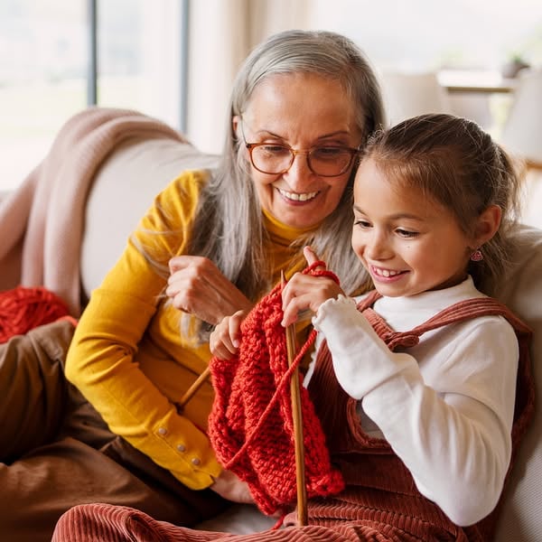 An ad in Meta's Ad Library: a grandmother in a yellow sweater knitting red wool with a smiling girl on a sofa
