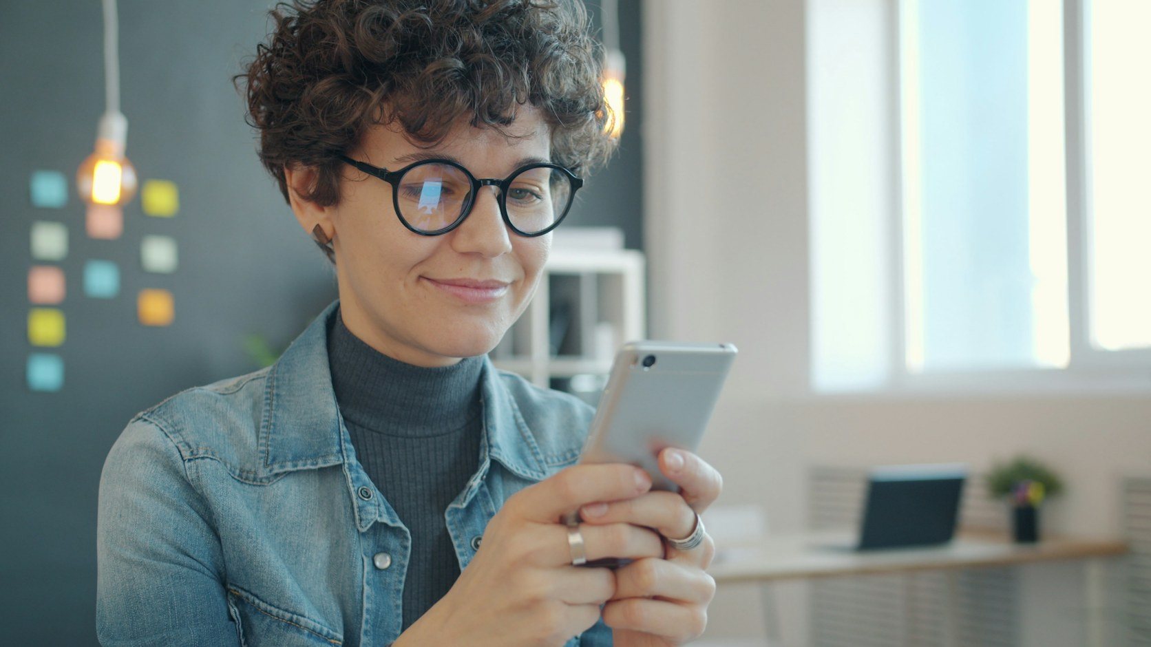 A woman in glasses smiling at her phone, the way most people meet a profile: highlights first
