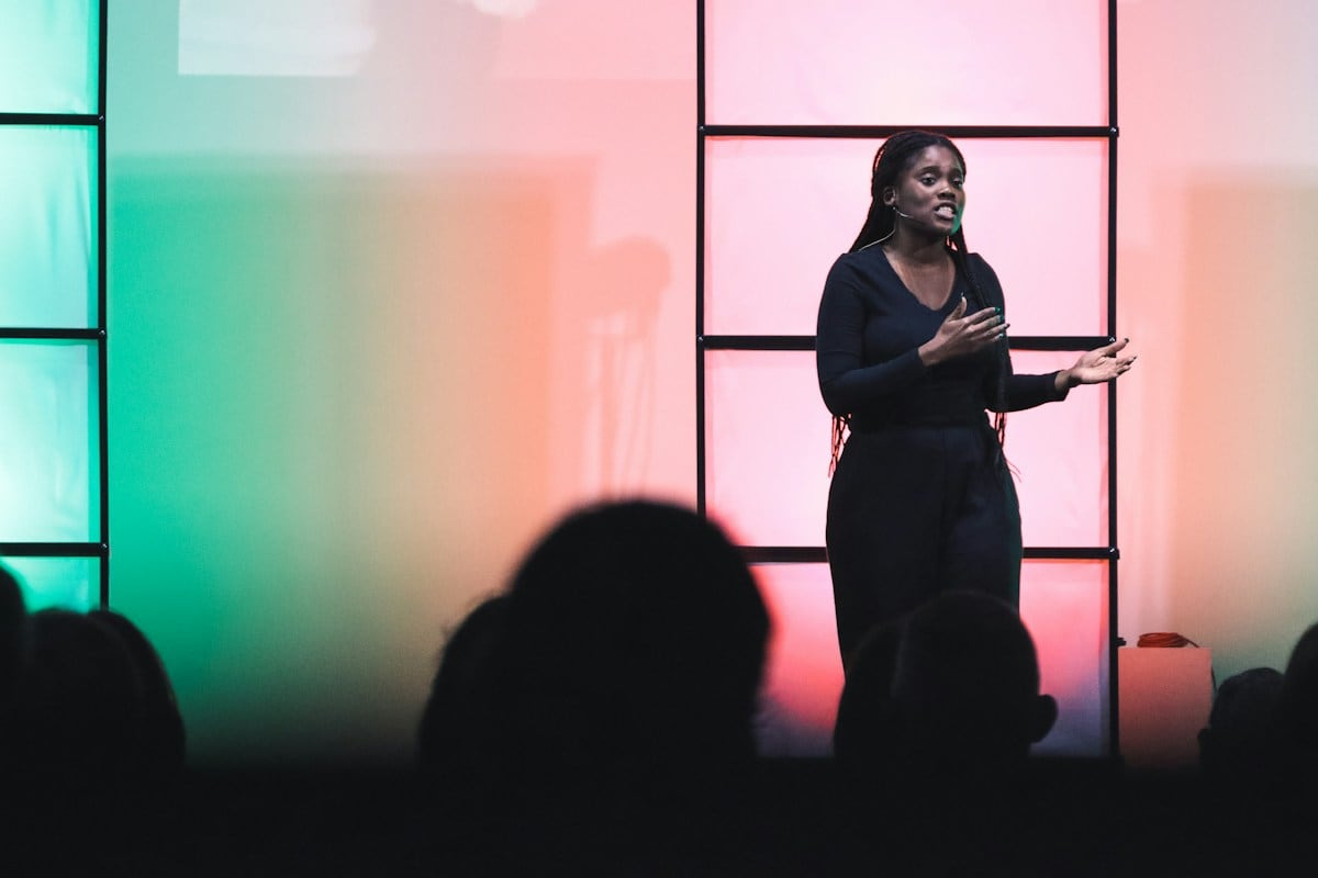 A woman speaking on a stage in front of an audience: a founder post works like a short talk, one decision or one number at a time