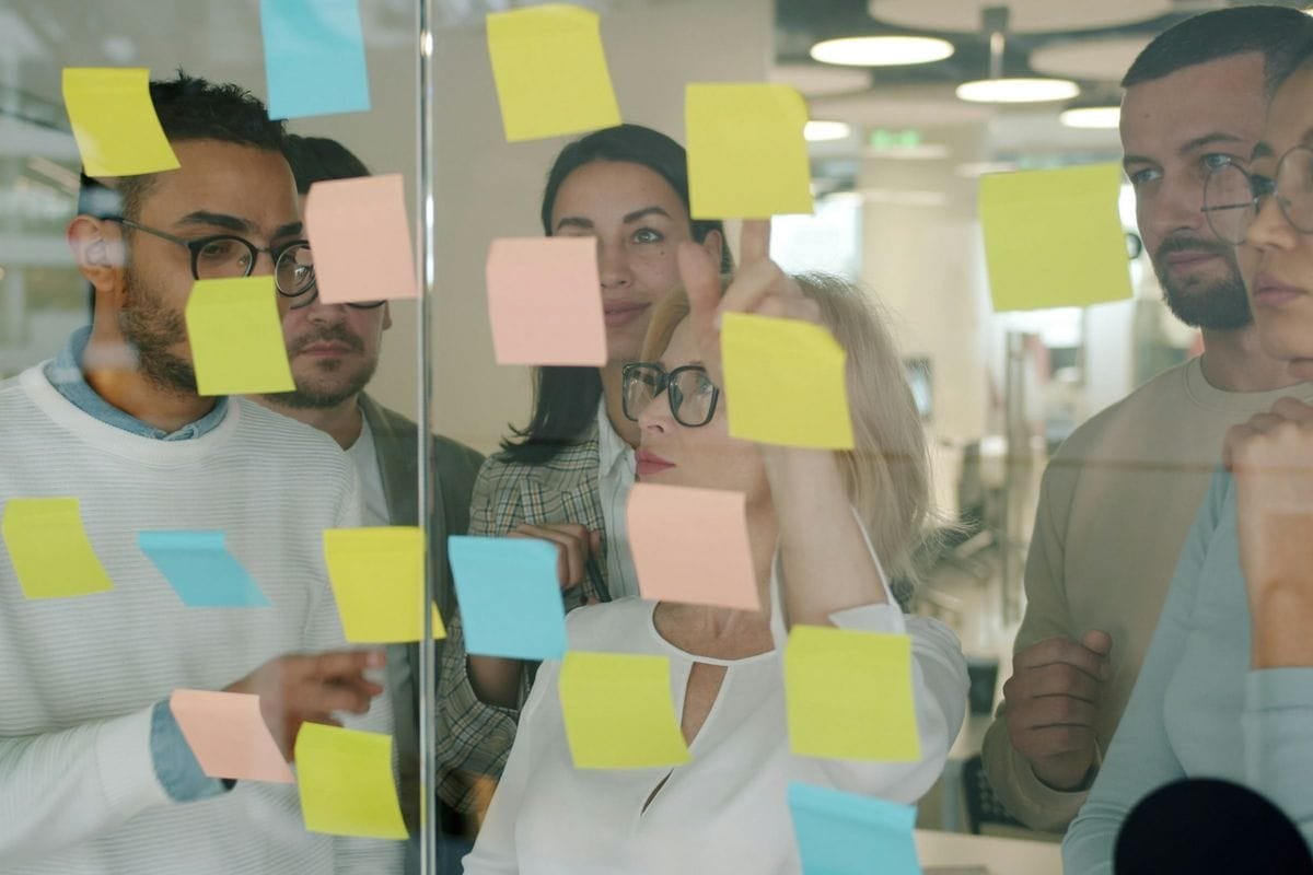 A team sorting colorful sticky notes on a glass wall: a posting week planned in one session, one idea per day