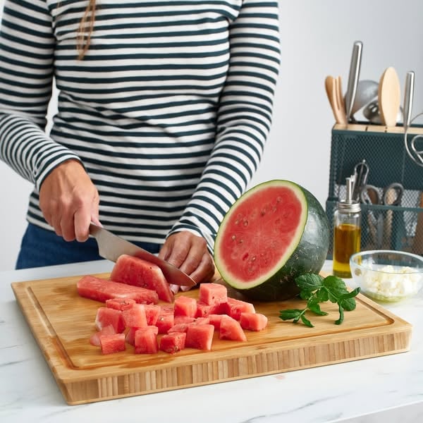 An ad by IKEA in Meta's Ad Library: Turn your vision into a dream kitchen, over a photo of a woman cutting watermelon on the APTITLIG bamboo butcher block