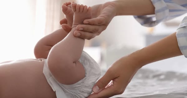A diaper ad in Meta's Ad Library: a parent's hands lift a baby's feet during a diaper change on a white sheet