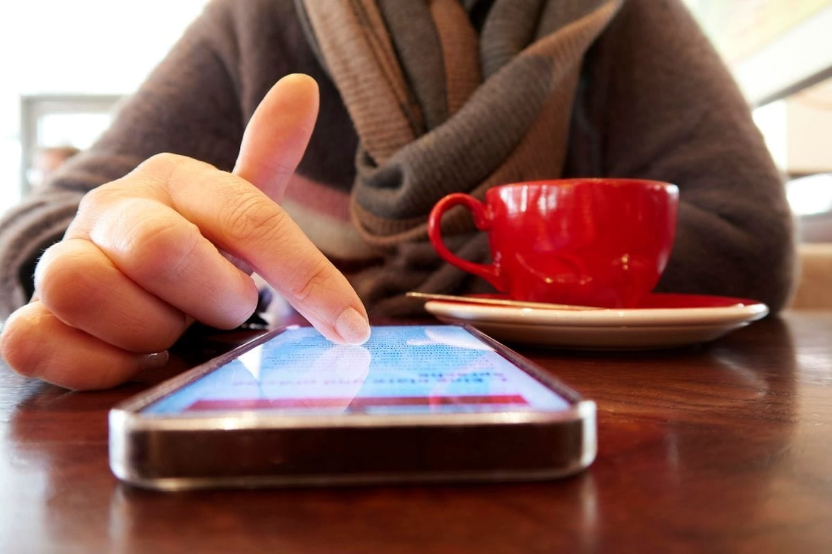 A finger scrolling a social feed on a phone next to a red coffee cup: a static ad has about a second in this scroll to make its point