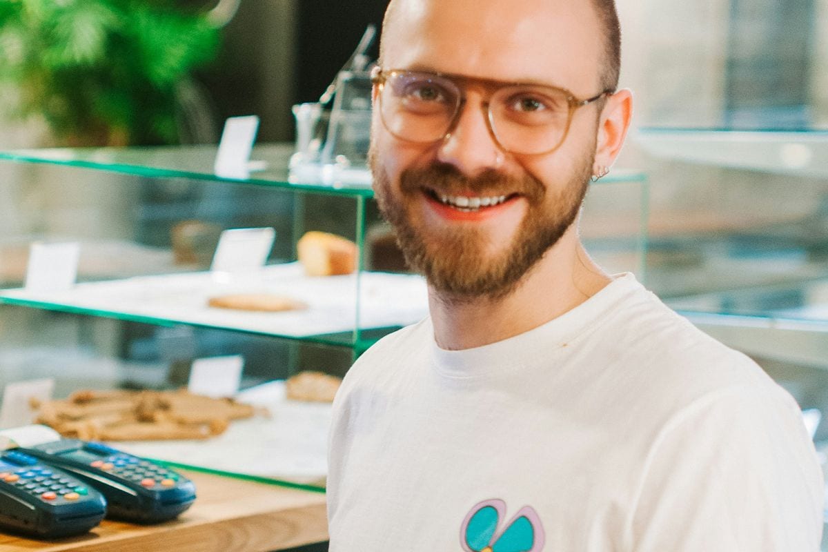 A smiling cafe owner talking across his counter next to the card reader: the person who serves customers is the face a trust video puts on the shop