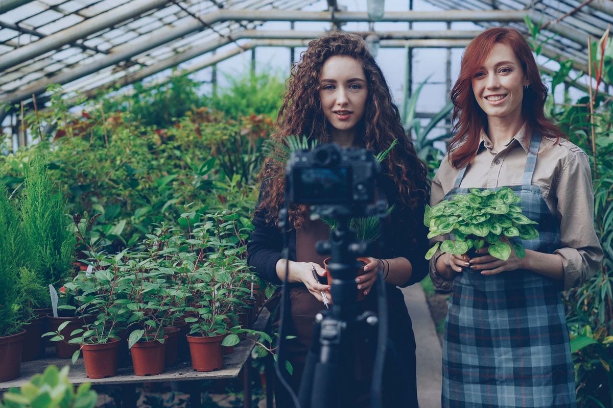 Two shop owners recording a video among potted plants in their greenhouse: the business itself is the set, no studio needed