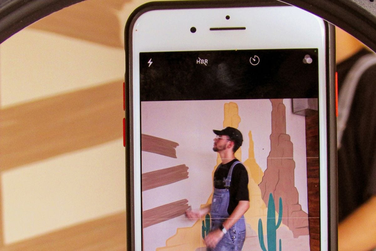 A phone held in a ring light records a take of a man in front of a painted wall: the setup most UGC creators shoot on, so judge the result on screen