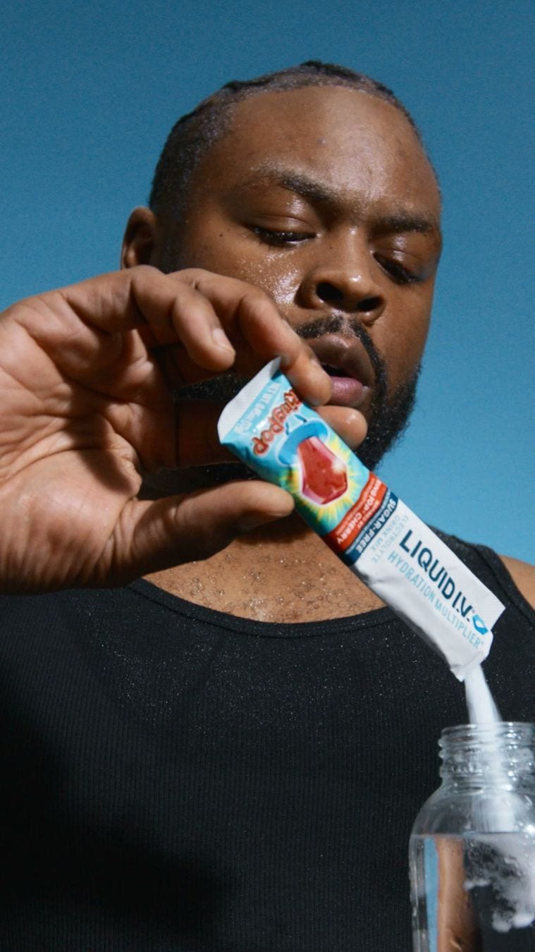 The opening frame of a Liquid I.V. video ad in Meta's Ad Library: a man tears a hydration stick and pours it into a water bottle against a grey wall