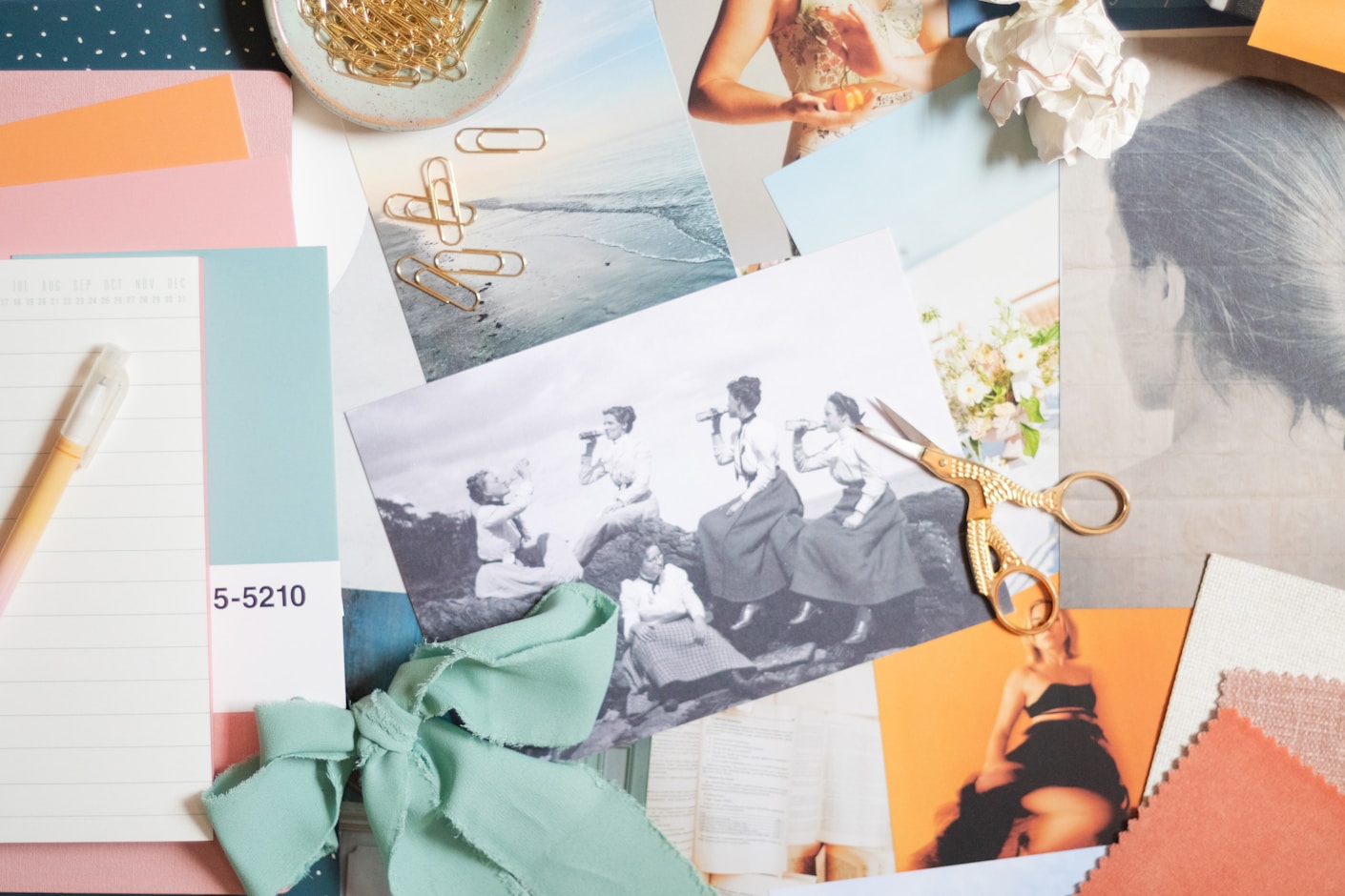 A brand moodboard laid out on a table: photo prints, coral and mint paper swatches, a ribbon and a pair of gold scissors